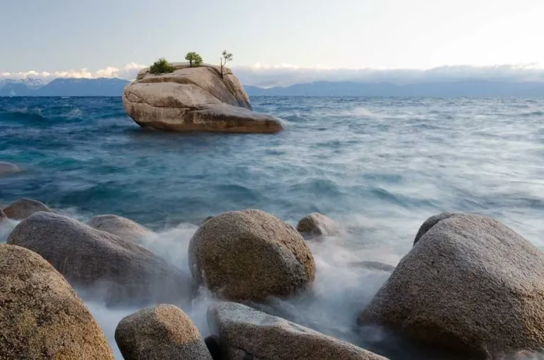 Waves moving along smooth rocks in a blue lake.