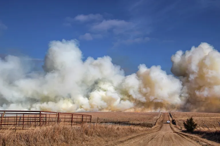 Large clouds of white smoke on dusty country road near brown fields