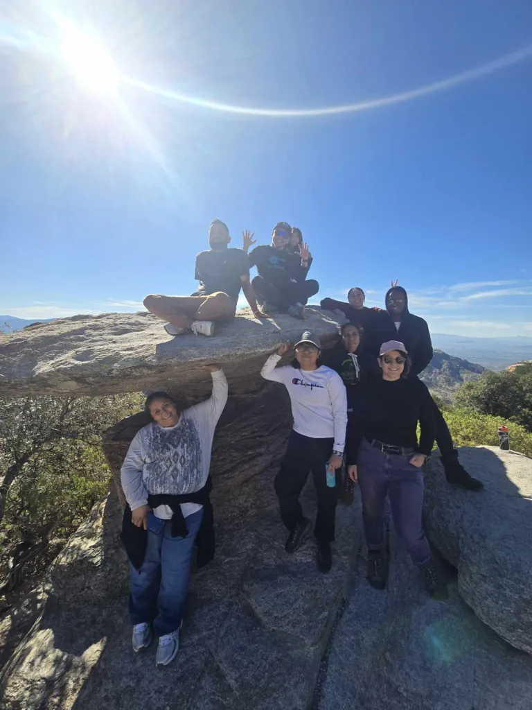 a group posing next to and on a large boulder