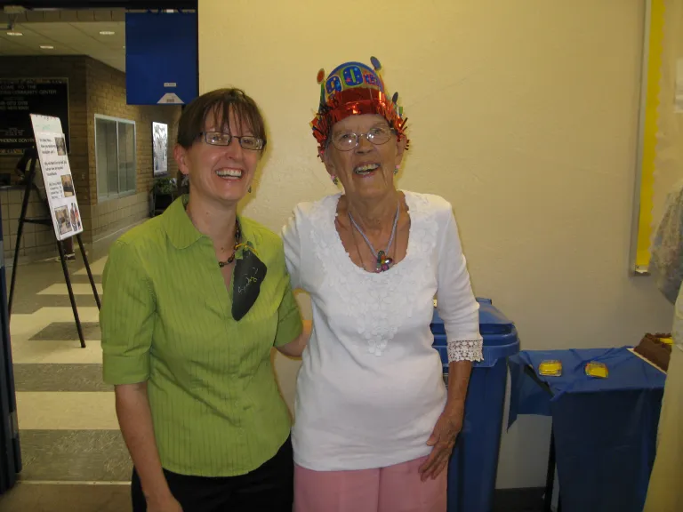 two people standing side by side, one wearing a birthday hat