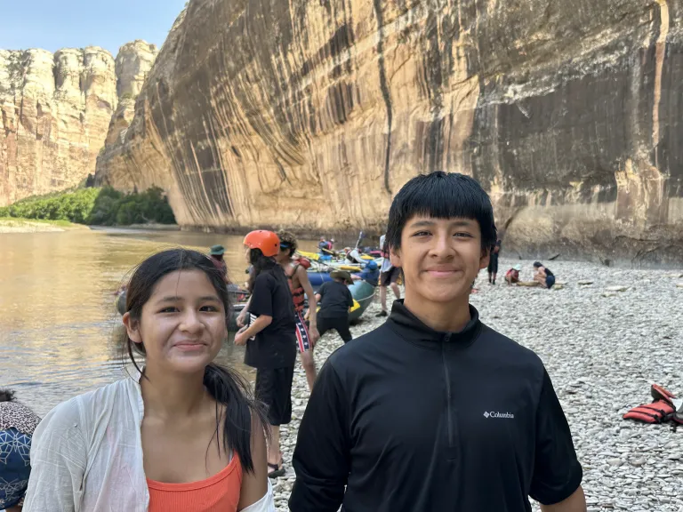 A photo of a teenage girl and boy in front of a river in a canyon 