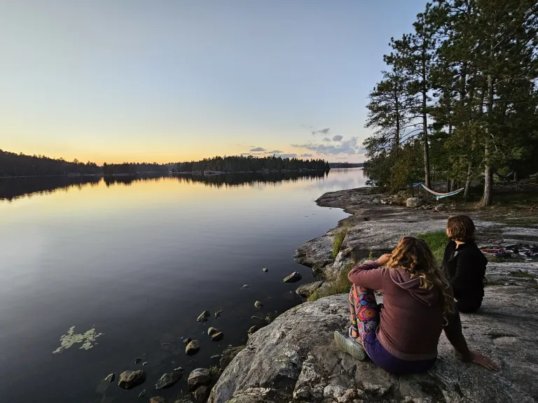 Friends looking into the sunset over a calm body of water.
