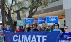 A small crowd gathered in front of a building with signs that say "Climate Can't Wait"