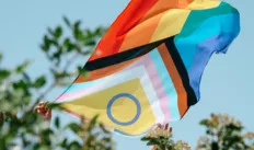 closeup of a man showing an intersex-inclusive progress pride flag peeping out from a bush