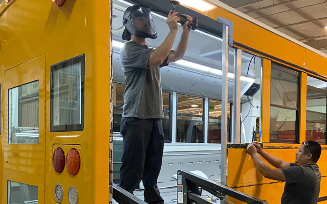 Two men retrofit a yellow school bus