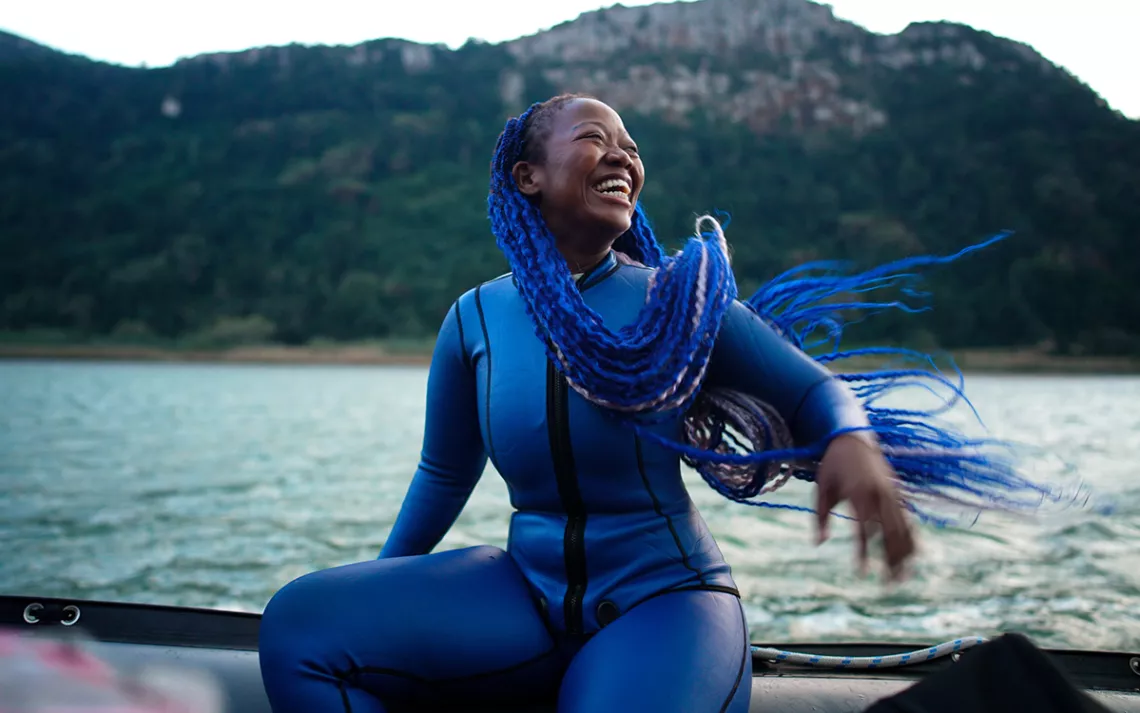 Still image from the film The Black Mermaid of a beyond fabulous Black woman with purple braids in a purple wetsuit. 