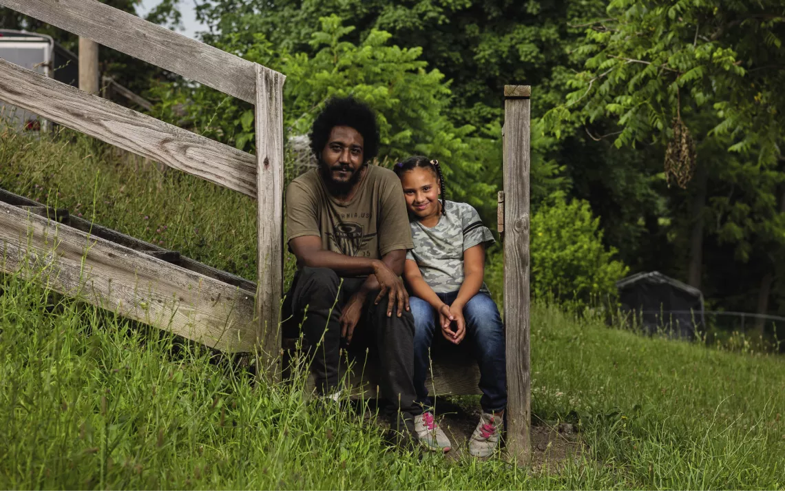 Jeff and Cheyenne Bryant sit close together on a wooden staircase surrounded by grass outside their home.