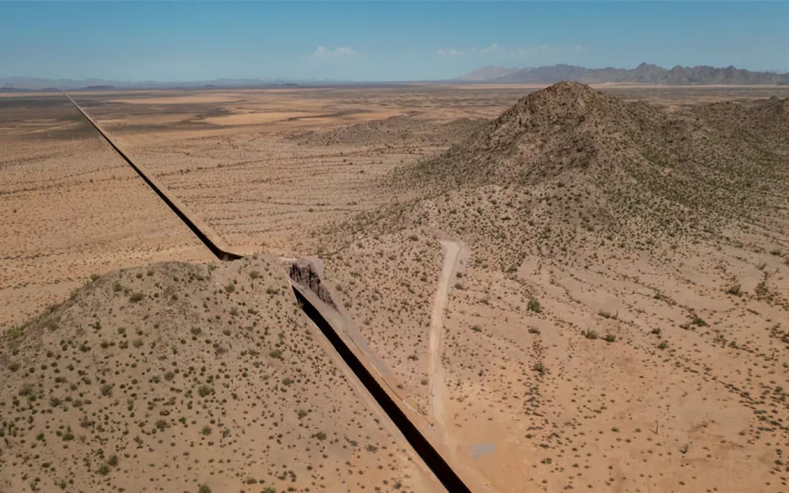 Aerial photo of a large stretch of border wall cutting through scrubby desert landscape.