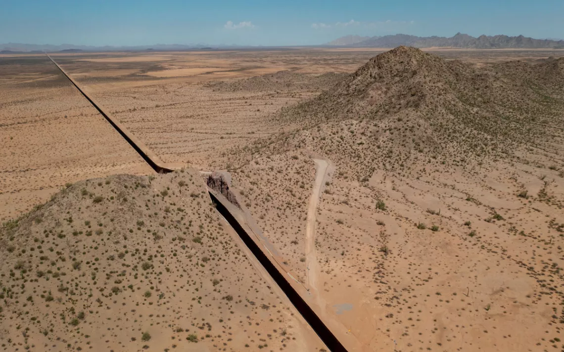 Aerial photo of a large stretch of border wall cutting through scrubby desert landscape.