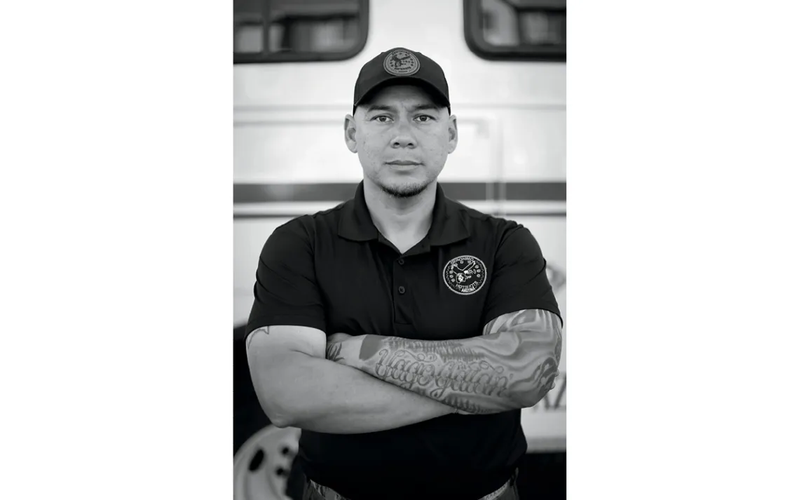 Julius Hostetler wears a black shirt and cap. His tattooed arms are folded in front of him.