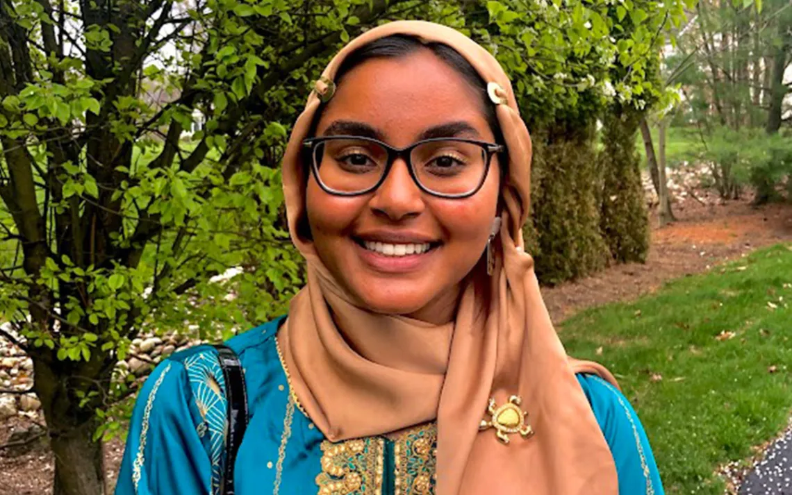 Photo of Khadija Shaikh, smiling, in a verdant wooded landscape. 
