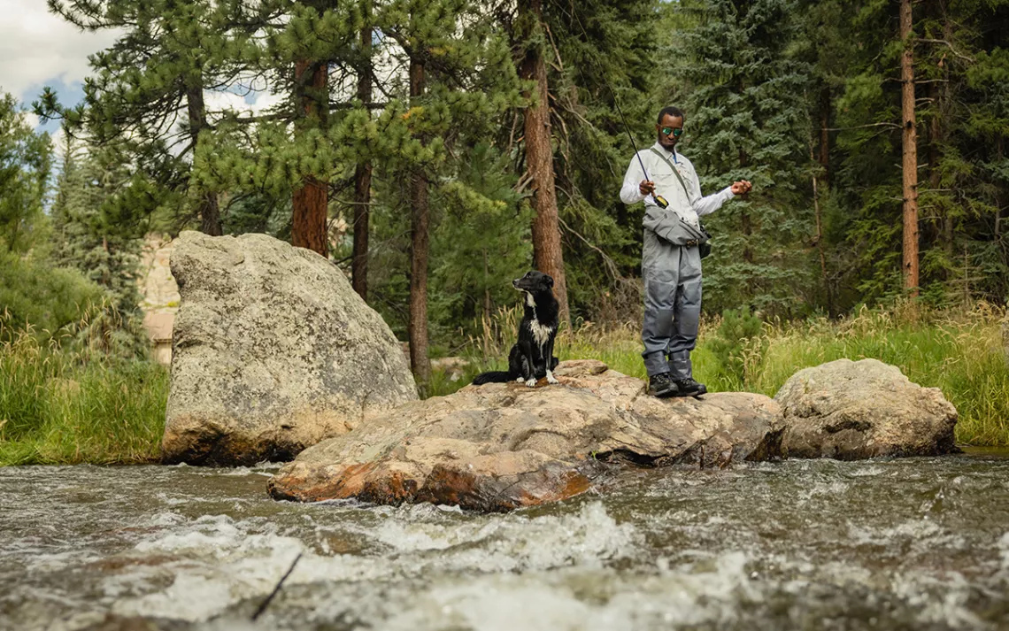 Eeland Stribling and his dog, Wilfred, stand on a rock while fishing in Bear Creek outside of Denver, Colorado..