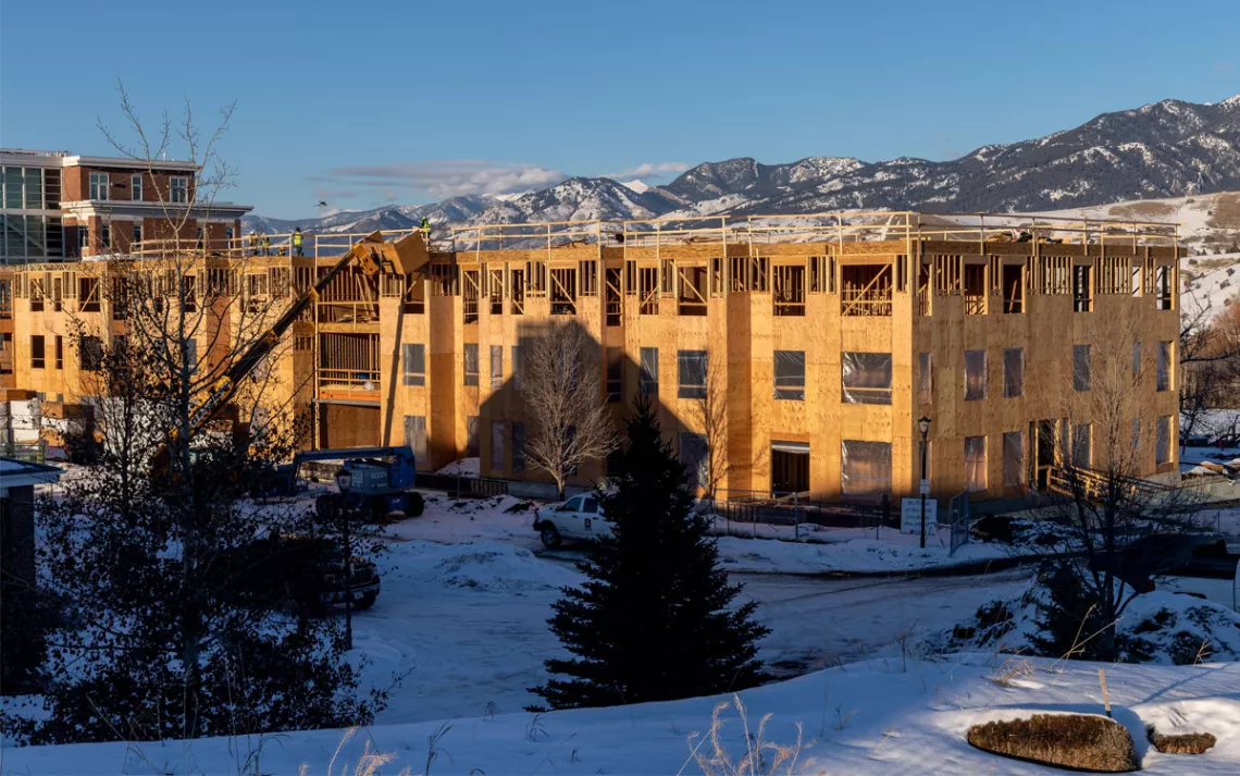 The exposed wood siding of a large commercial building under construction, with mountains in the background.