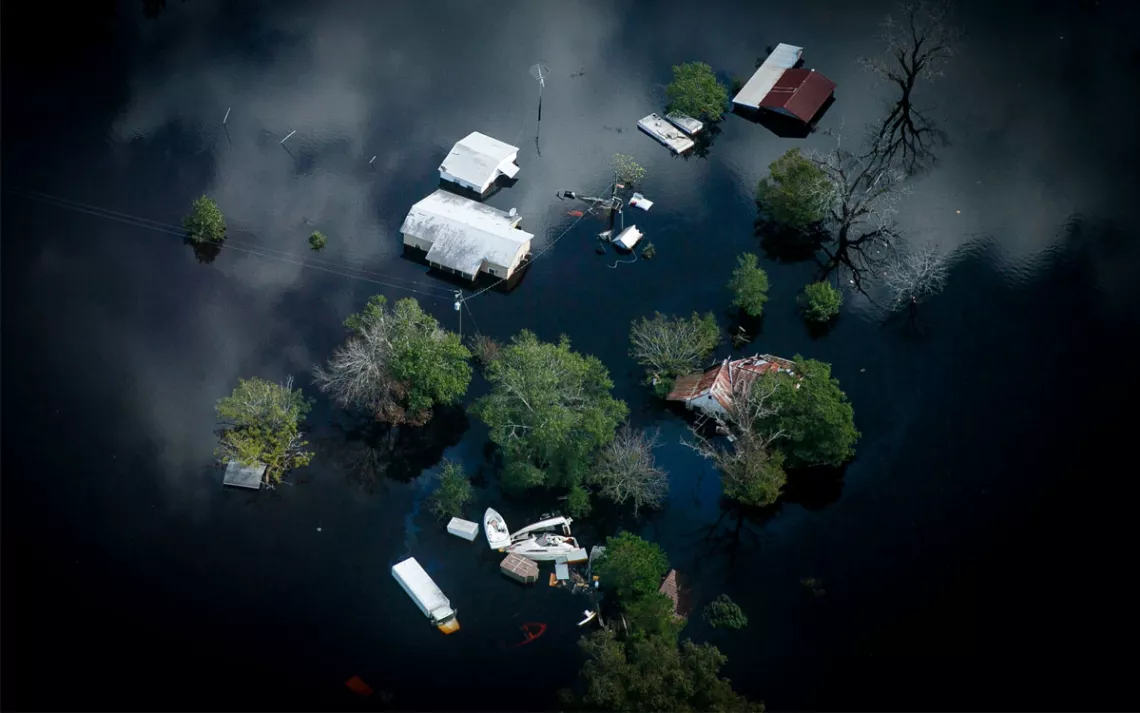 Overhead photo shows houses almost completely submerged in water, treetops, and floating items.