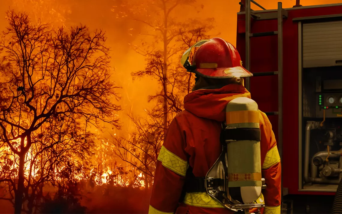 Firefighter extinguishing wildfire with fire truck. Photo by Toa55 | iStock
