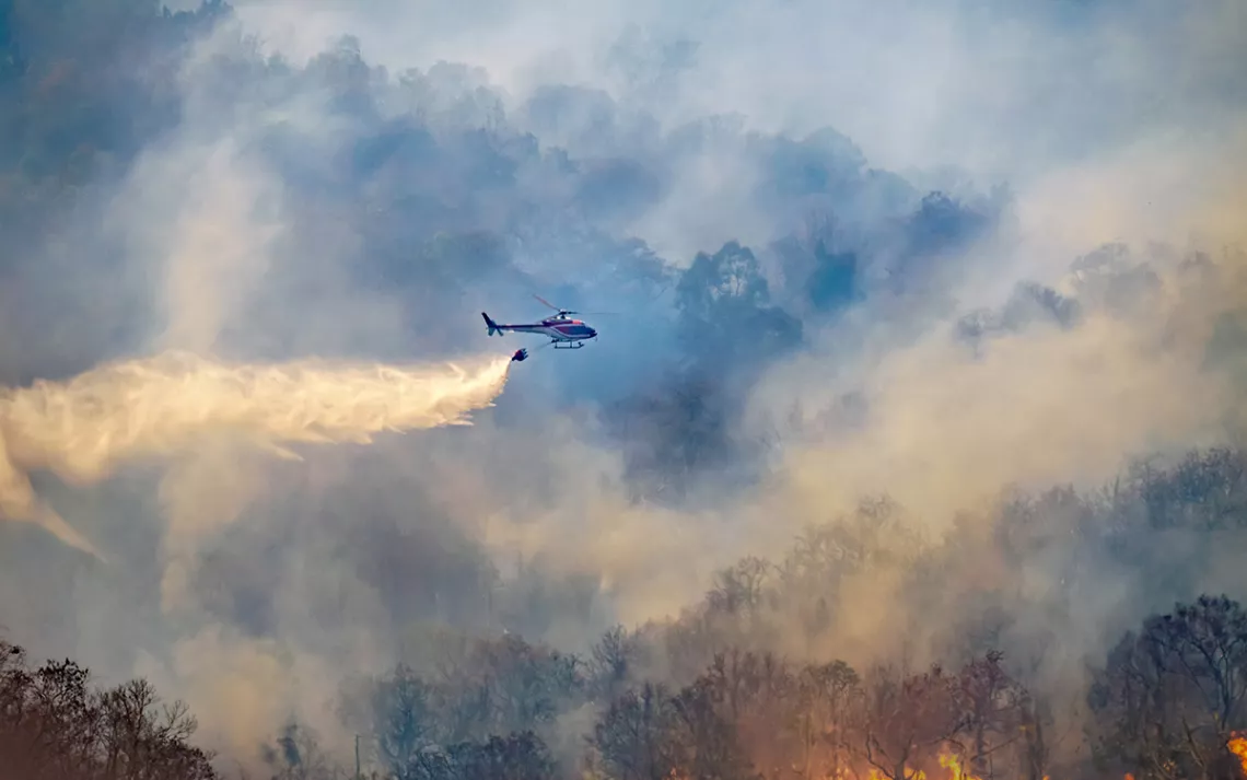 Helicopter dropping water on forest fire. | Photo by Toa55/iStock