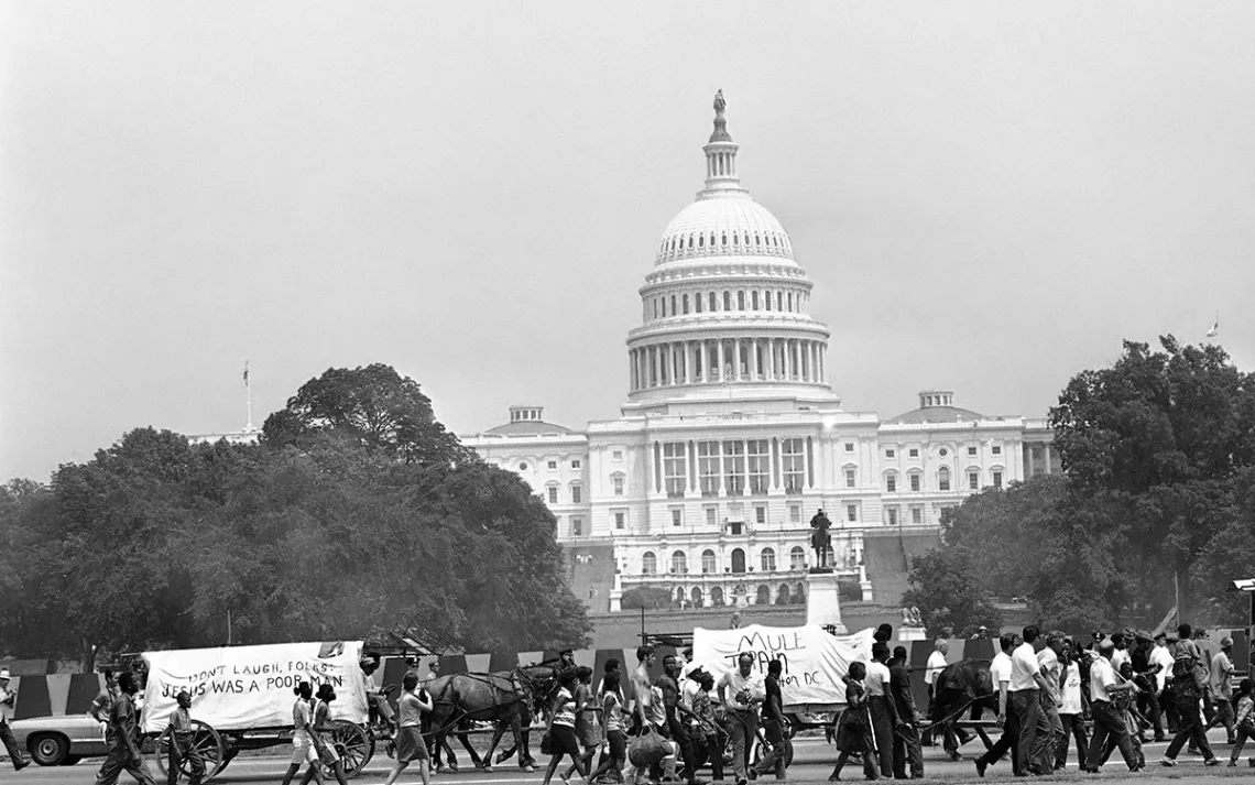 People walk along beside two wagons of the mule train of the Poor People’s Campaign as it makes its way down First St. N/W., past the U.S. Capitol Building.