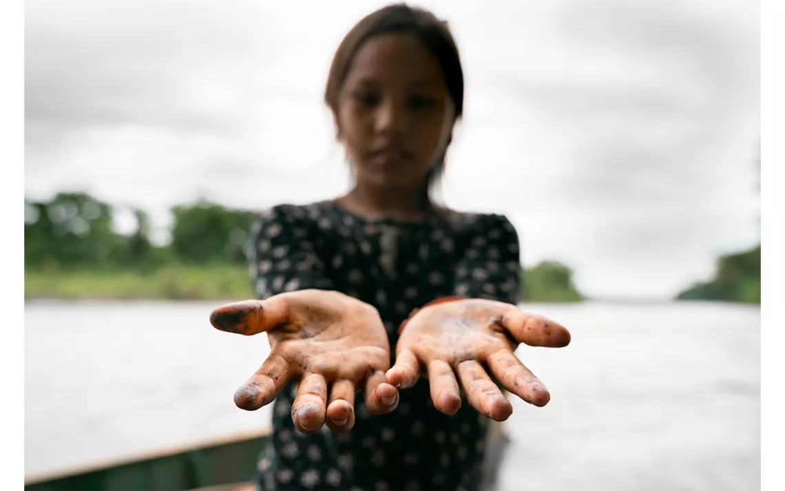 An Indigenous girl’s hands are stained from crude oil after playing along the riverbanks near the community of San Pedro de Río Coca, northern Ecuadorian Amazon, April 18, 2020. 