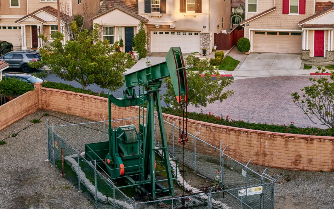 An oil drill is next to a cul-de-sac of a suburban neighborhood.