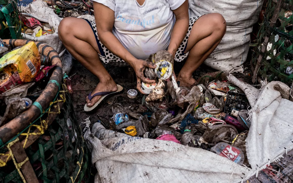 A pregnant woman sorts through garbage in front of her shack. When women can no longer collect trash, they often help their families by picking through bags of materials.