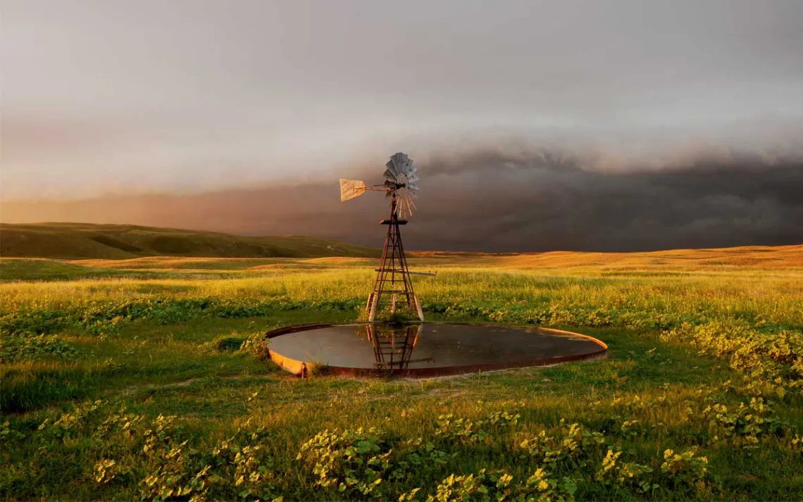 A small windmill sits above a shallow water tank in a grassy meadow.