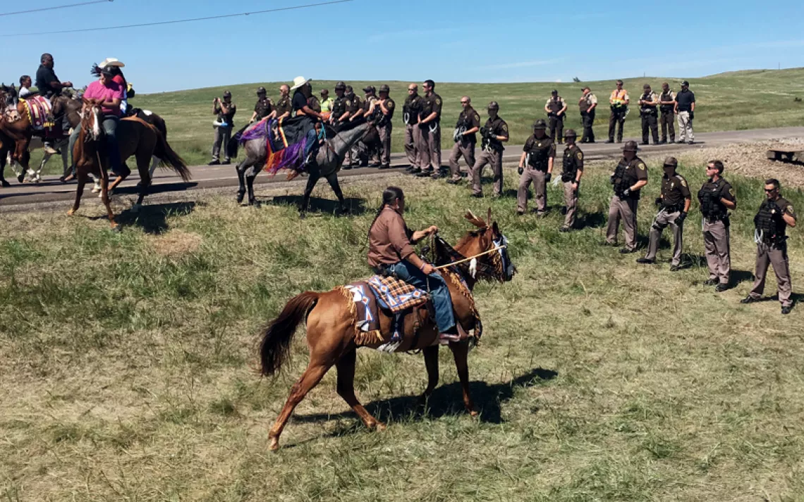 A row of Native Americans on horseback face off against a line of North Dakota police officers near the Dakota Access Pipeline
