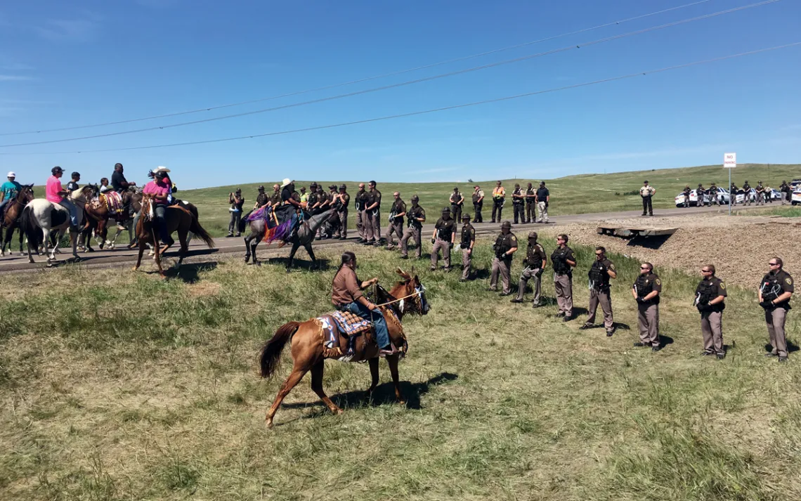 A row of Native Americans on horseback face off against a line of North Dakota police officers near the Dakota Access Pipeline