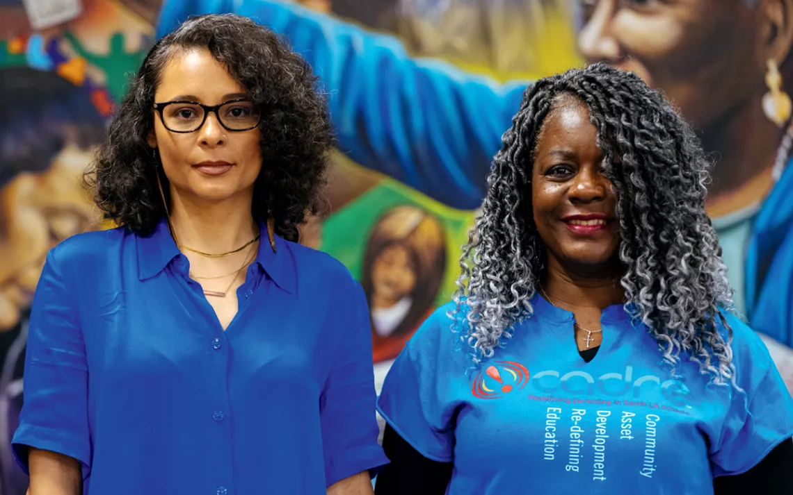 Élice Hennessee and Roslyn Broadnax stand side by side wearing blue shirts and looking at the camera.