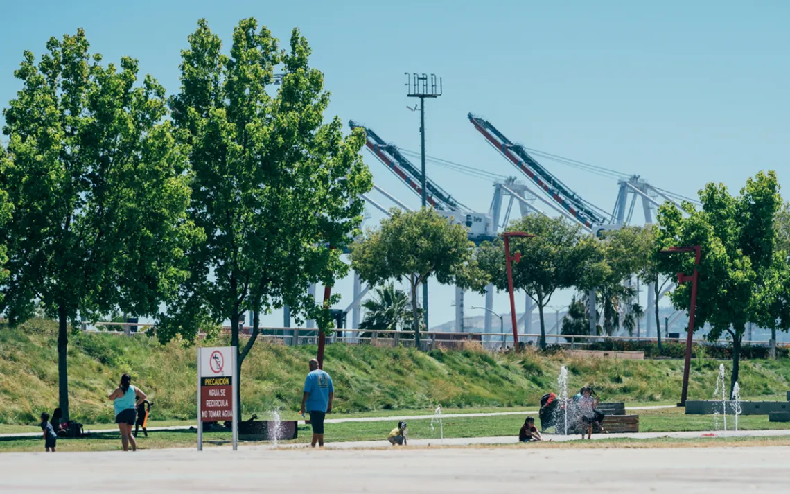 People gather on a stretch of greenery with fountains in front of the port.