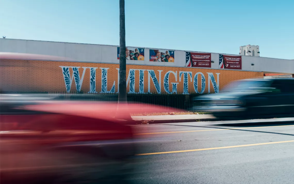 Cars drive past a mural that says "Wilmington" in orange, black, and white.