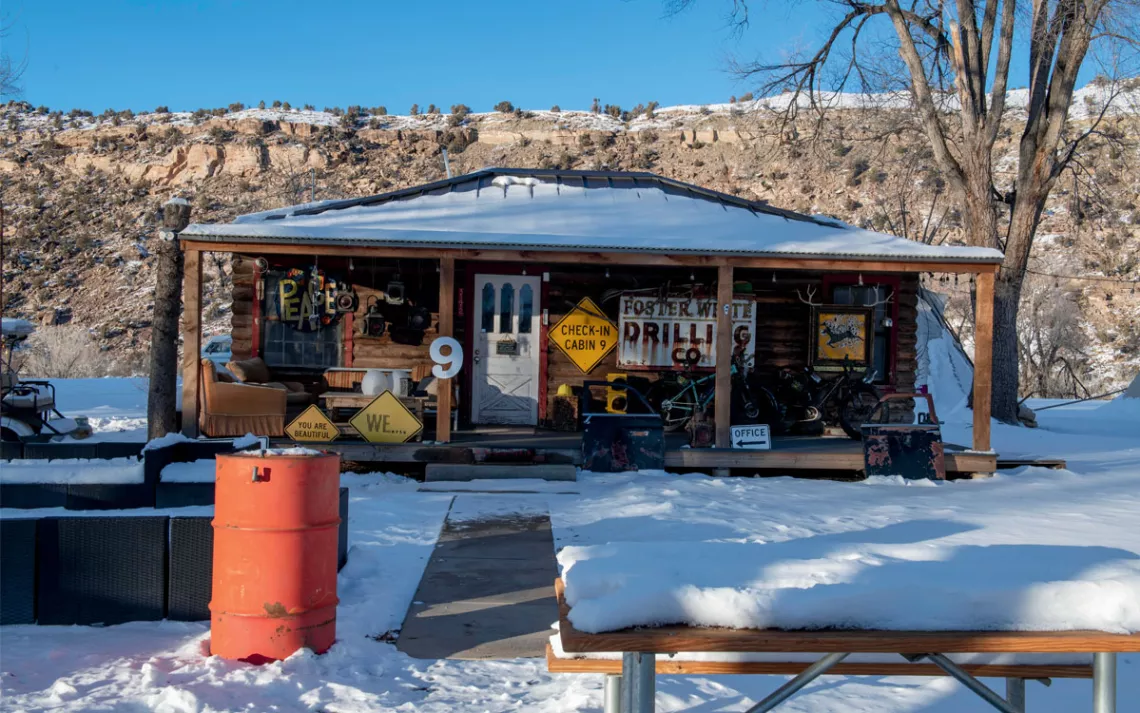 A squat wooden Camp V. glamping cabin is decorated with several old signs like "Foster White Drilling Co"