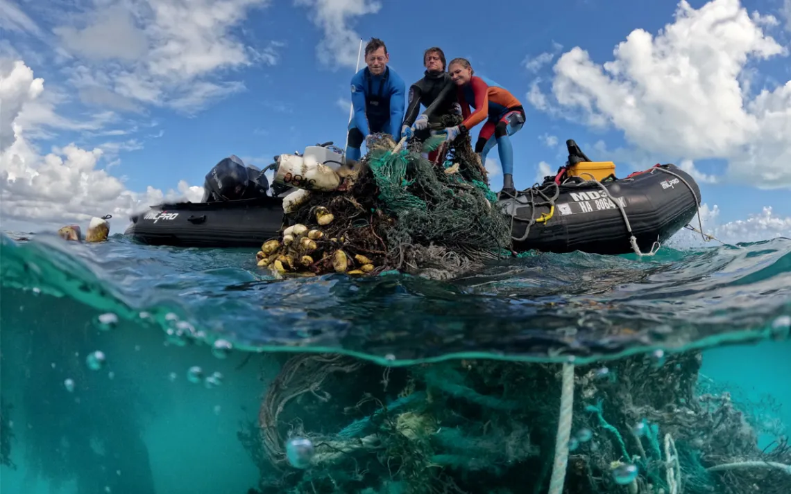 Kevin O'Brien and two others pull a huge tangled net out of the ocean into a dinghy.