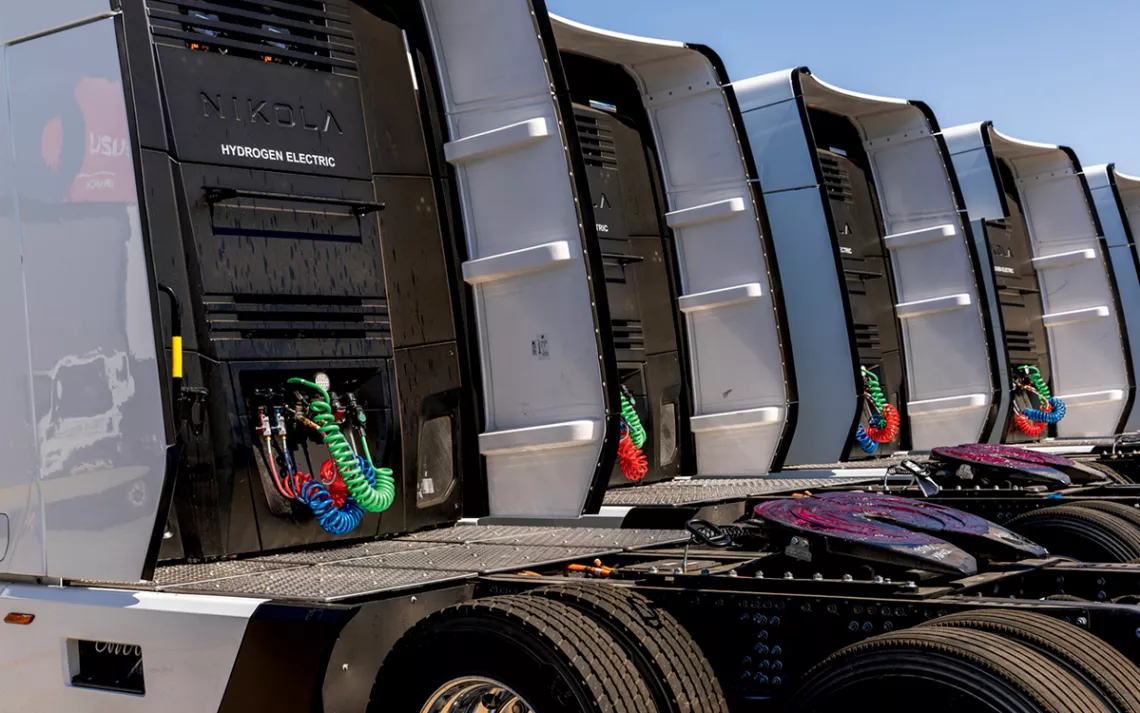  The cabs of several hydrogen electric trucks lined up, with green, blue, and red cords