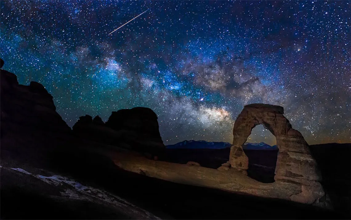 The Milky Way over a red rock arch. 