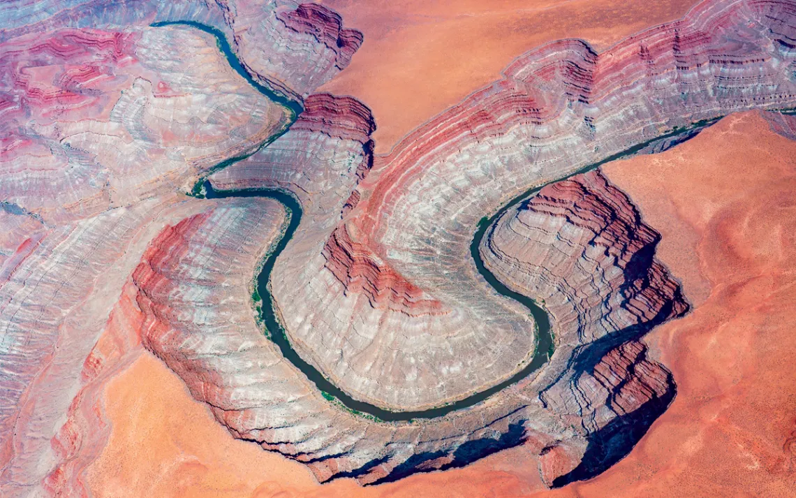 Aerial view of the San Juan River curving in a horseshoe. Surrounding it is a red, orange, and white rocky landscape.