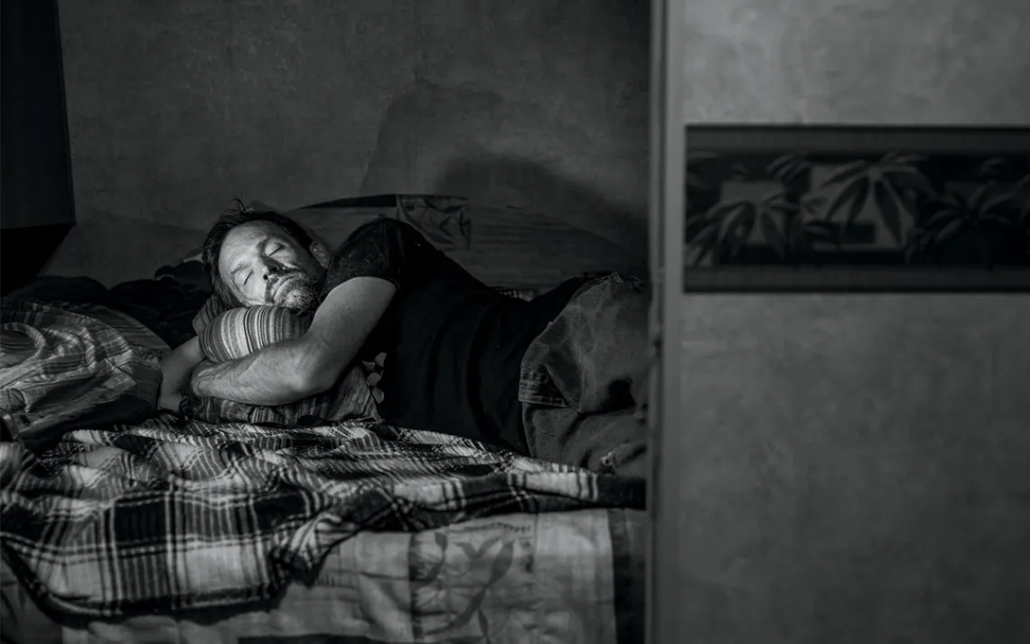 Nick Fischer lies on his bed and hugs a pillow with his eyes closed.