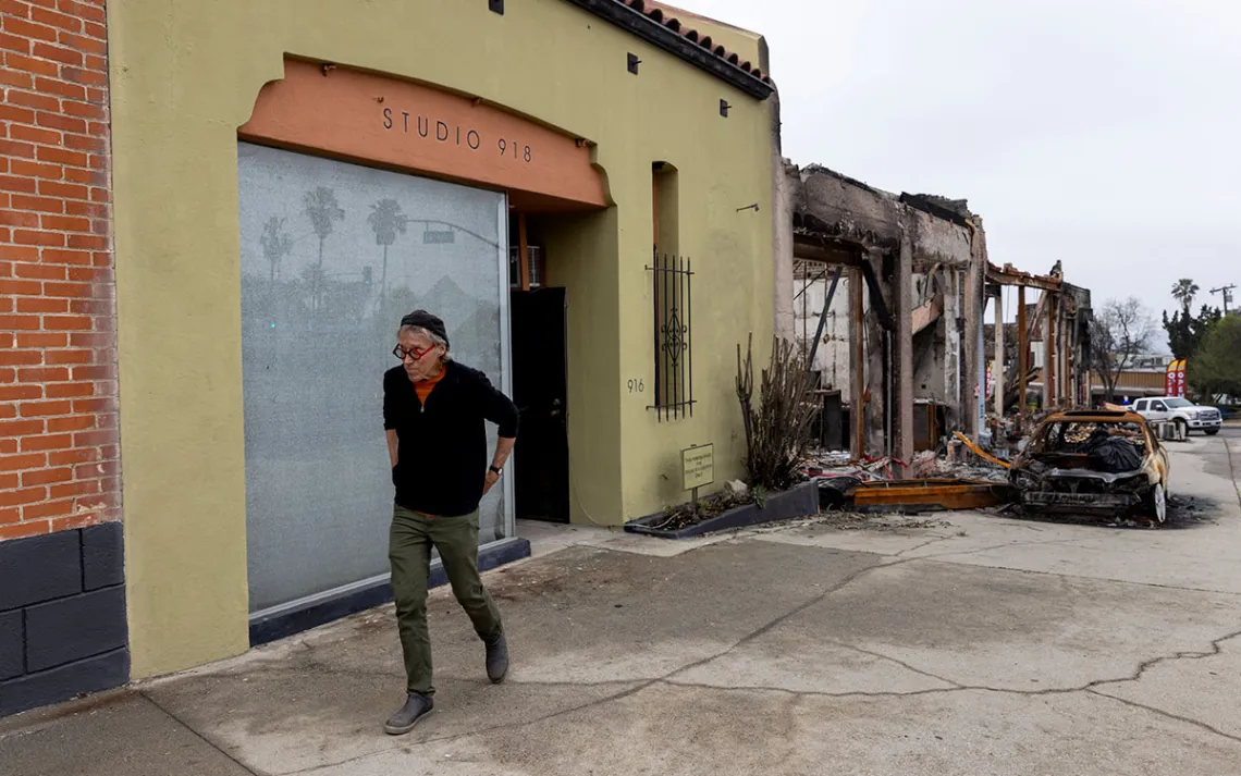 A man walks in front of his intact art studio, which is next door to a burned building