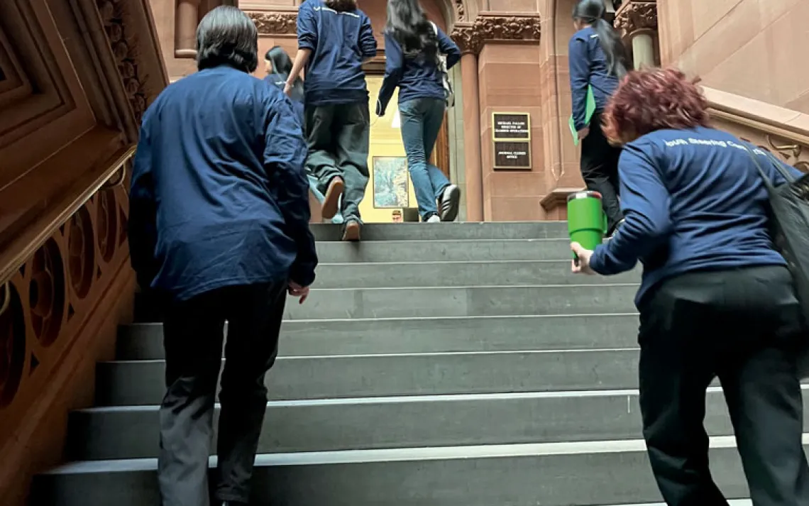 Students and adults from CRETF wearing black pants and dark-blue tops walk up the steps of the New York State Capitol.