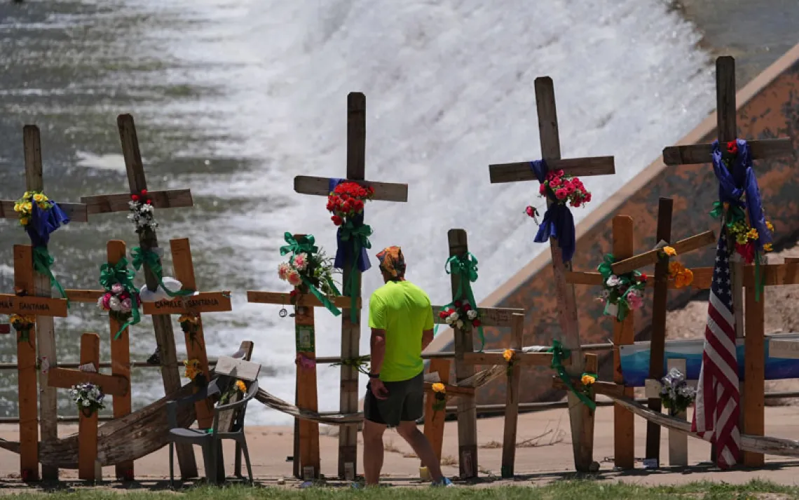 A man walks past crosses and flowers that form a make-shift memorial along the Guadalupe River as the Texas Senate and House Select Committees on Disaster Preparedness and Flooding hold a public hearing in Kerrville, Texas