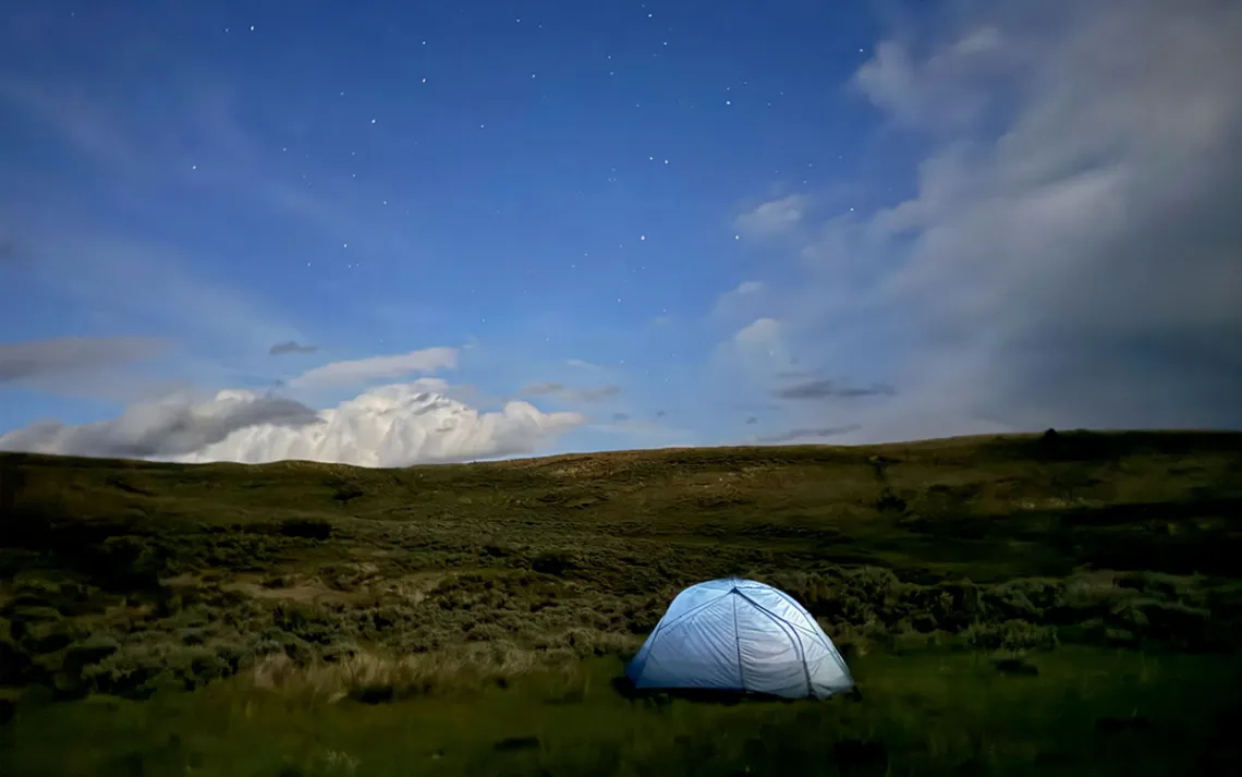 A round silver tent on a flat area of the Red Desert during dusk or dawn.