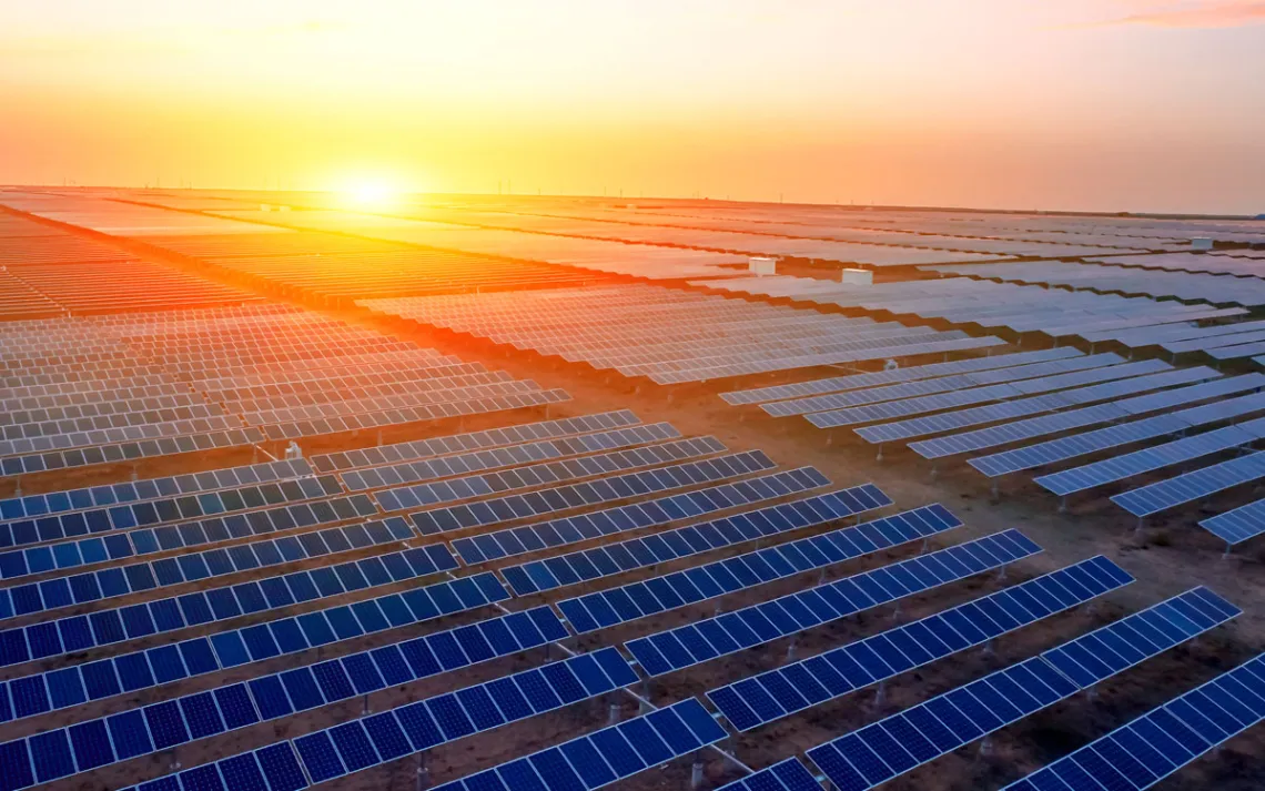 A large array of solar panels with the sun setting in the background.