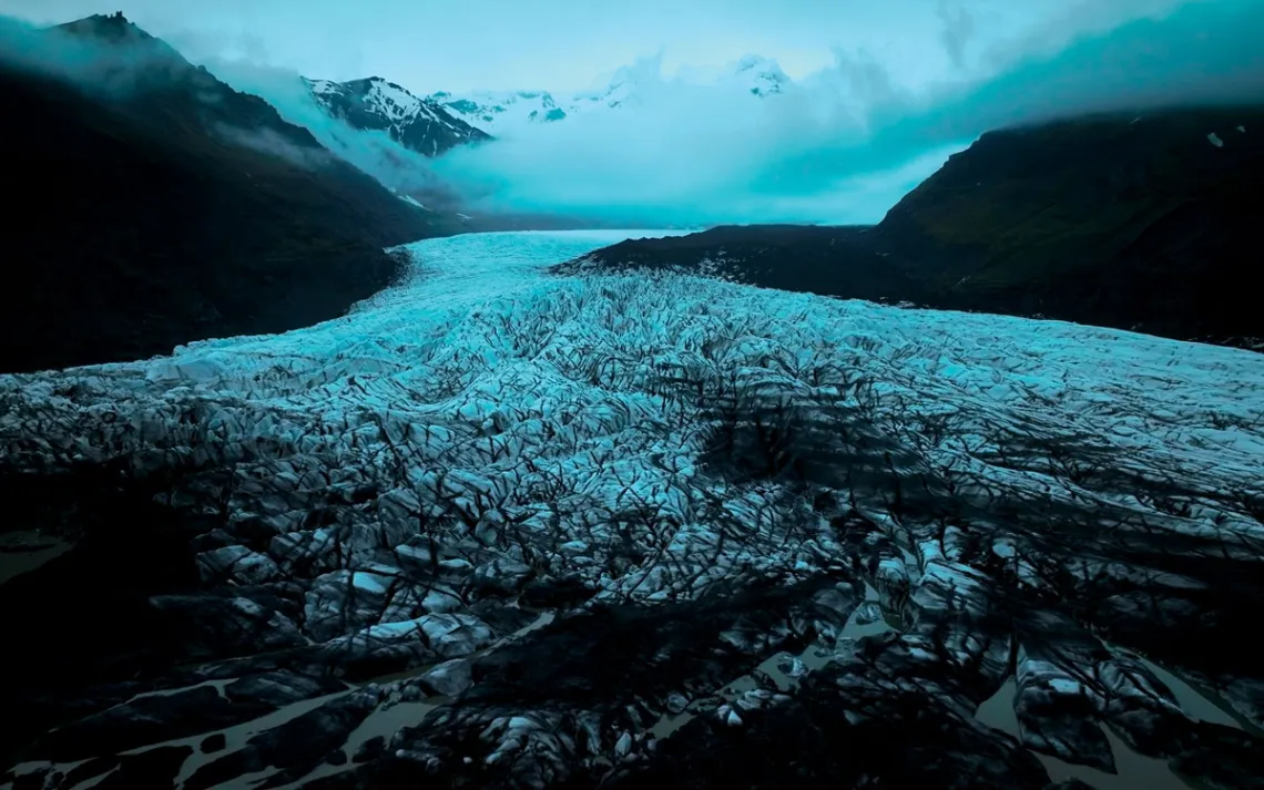 A dark sky and mist appear above the mountain and ice of Svínafellsjökull glacier in Iceland.