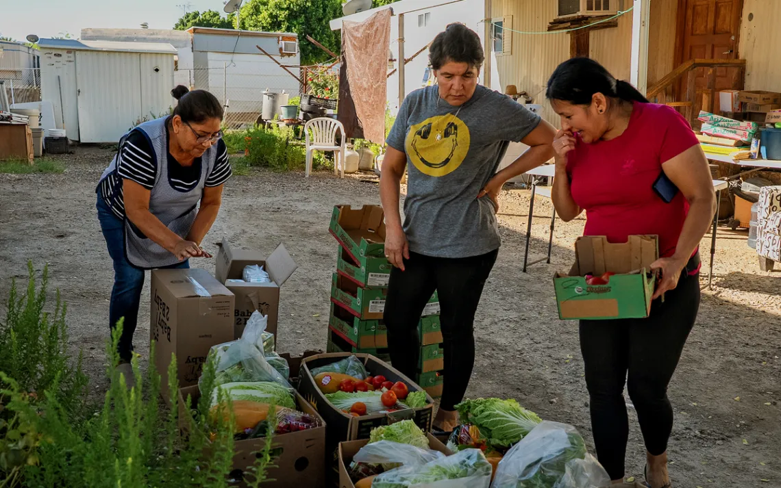 Casimira Tranquilina, Rosalba Ortiz, and Marisela Monetor pick out vegetables and fruit from boxes in front of some trailers.