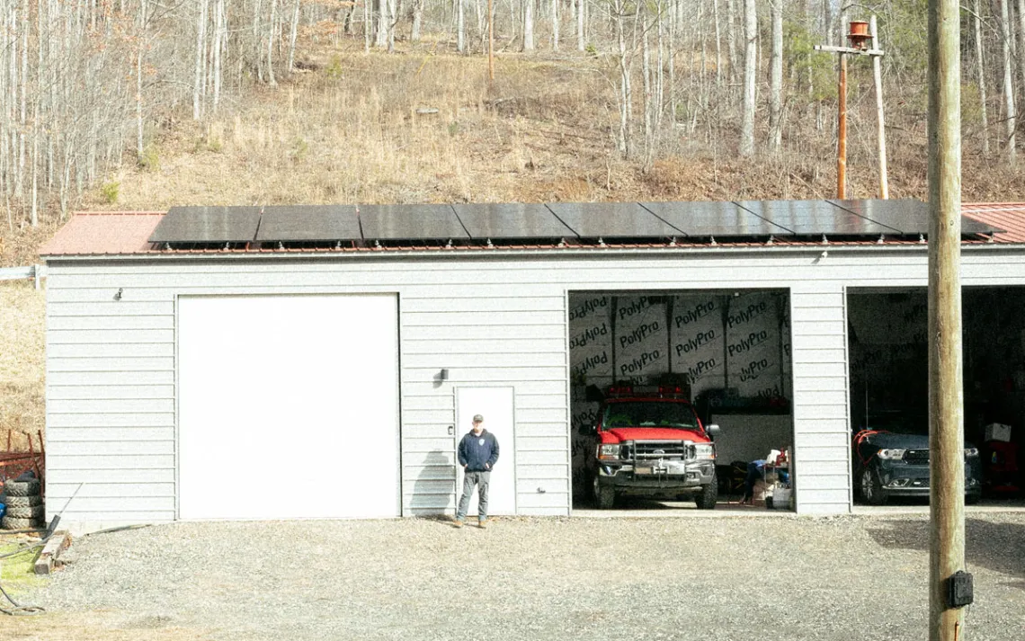 A man stands before a fire department building with solar panels affixed to the roof. 
