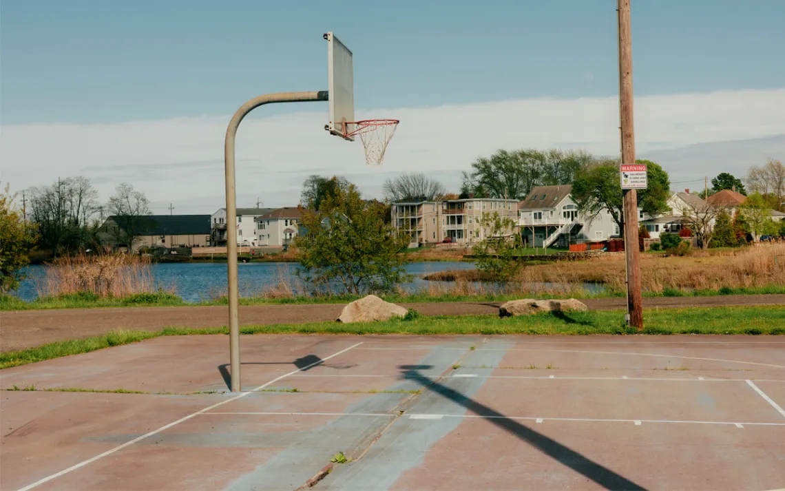  A basketball court at water level with houses lined along the shore.