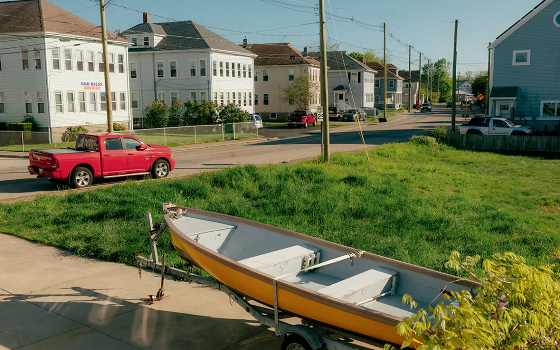  A boat sits in a slightly flooded driveway next to a road with large buildings lining it.