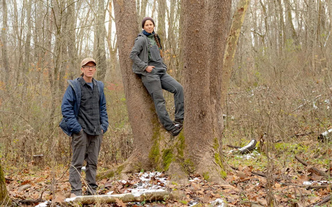 ressed for cold weather, Weston Lombard stands next to a tree and Molly Jo Stanley leans against it in a leafless-tree forest setting.