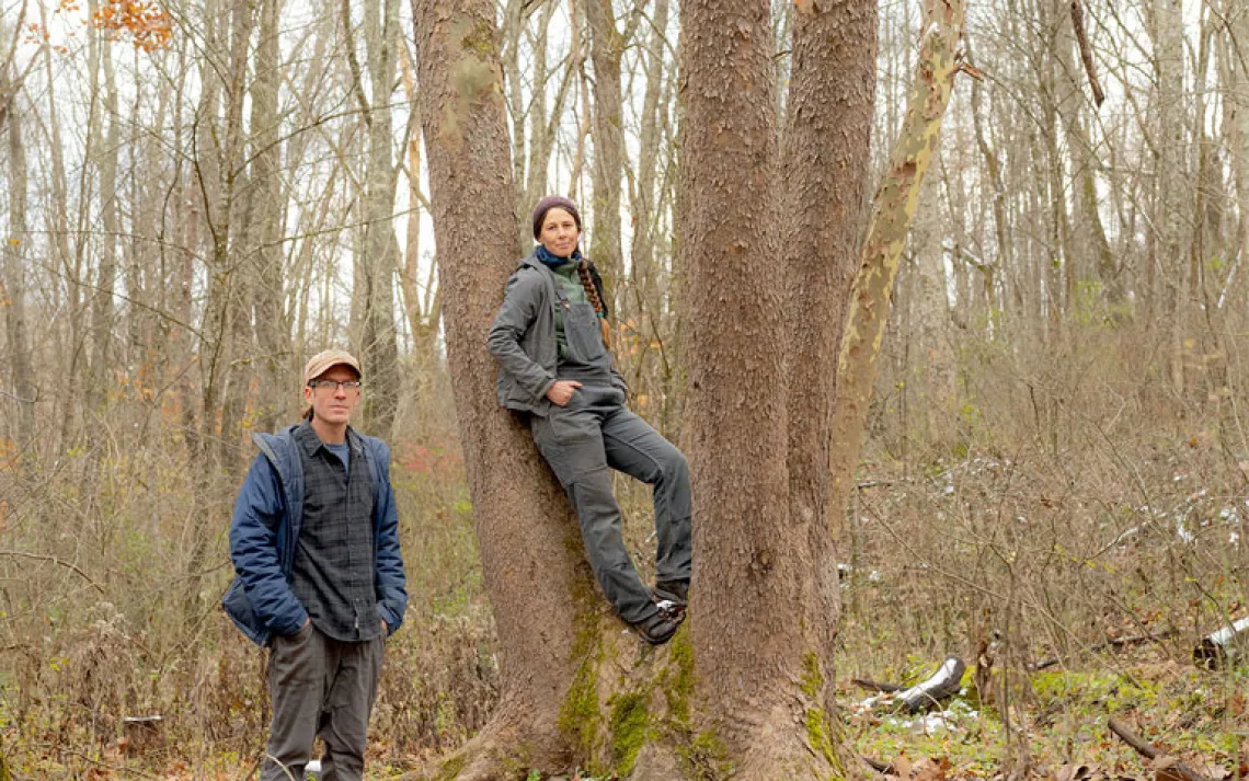ressed for cold weather, Weston Lombard stands next to a tree and Molly Jo Stanley leans against it in a leafless-tree forest setting.