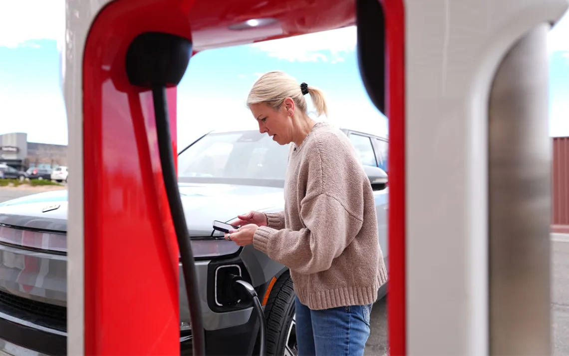 A driver, seen through an EV charging station, powering her EV SUV.