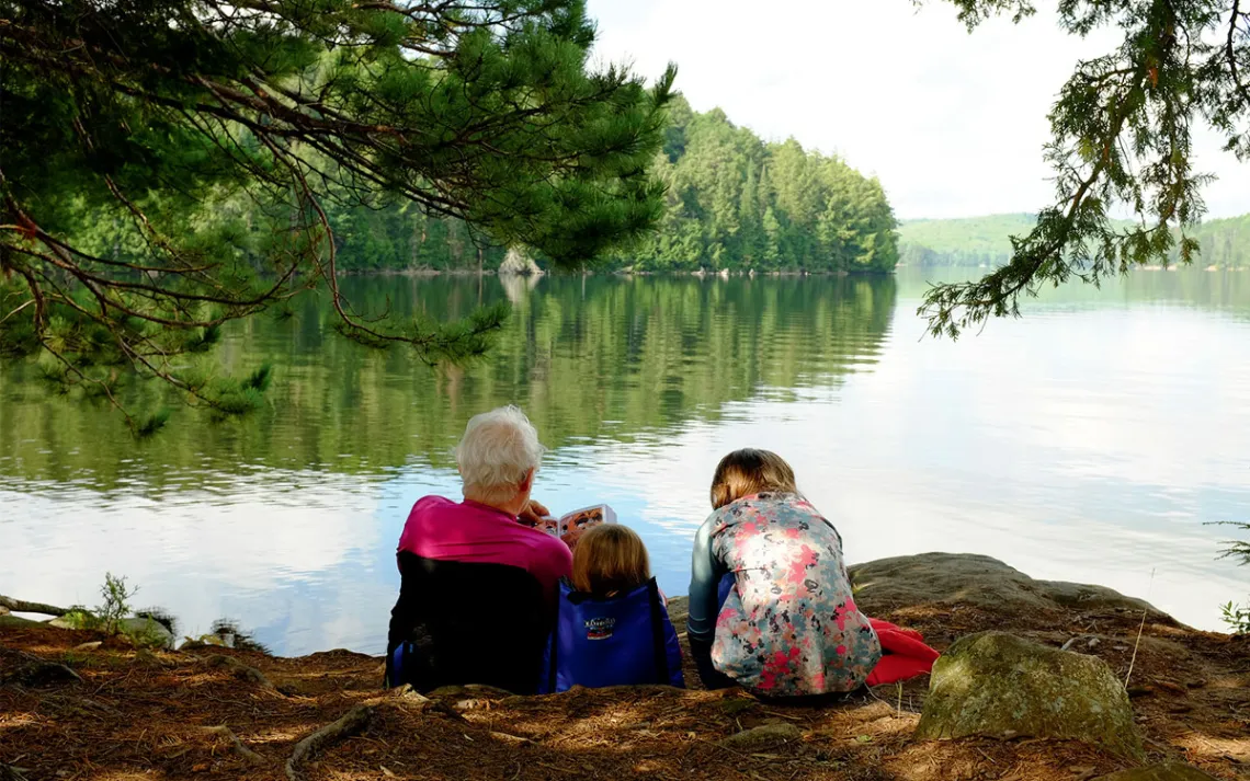 The backs of a grandfather and two children as he reads to them by a lake